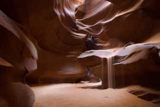 Slot canyon interior with sand sliding down a lit wall